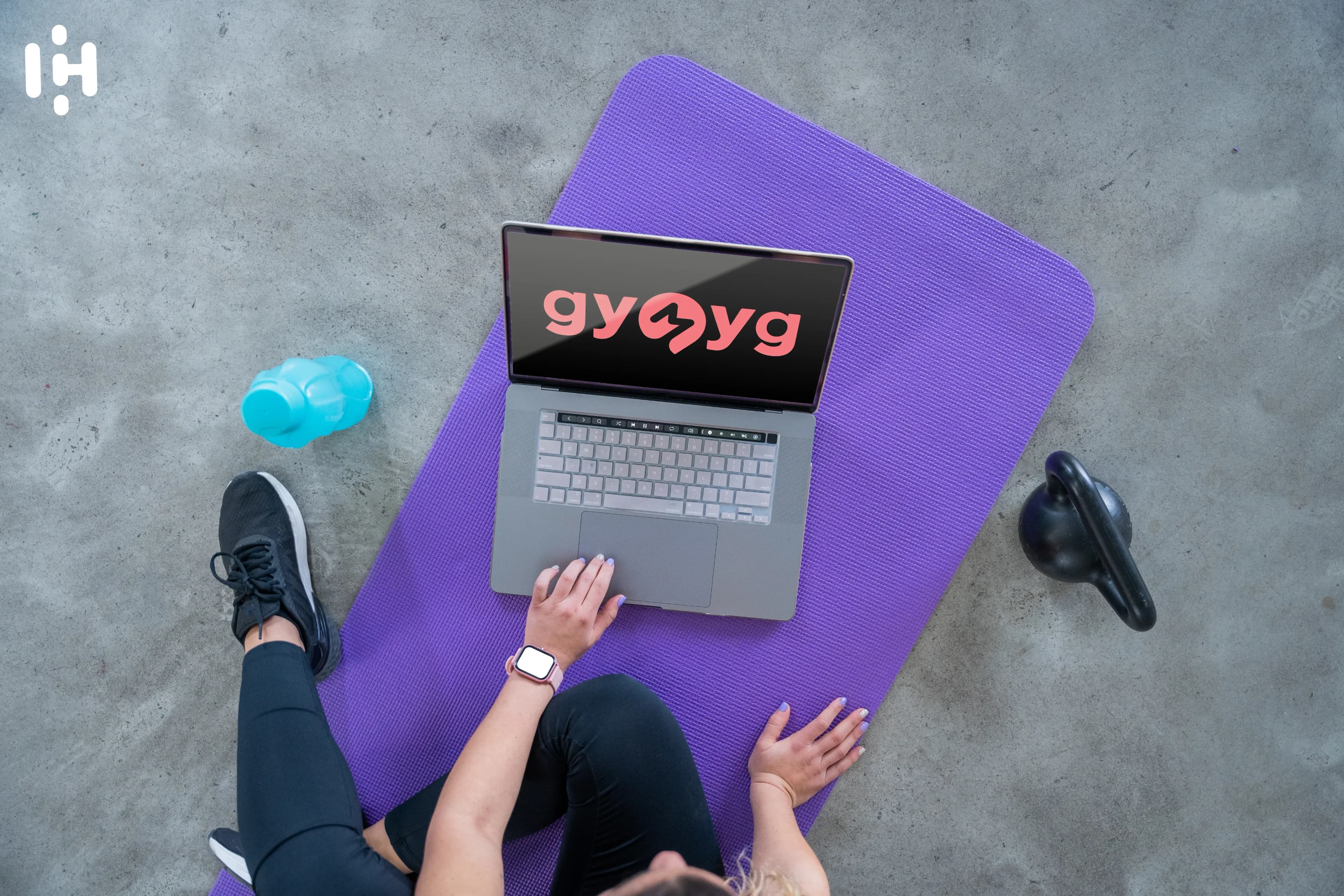 Person sitting on yoga mat using a laptop with GYMYG logo
